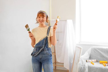 Odada boya fırçalı genç bir kadın var.