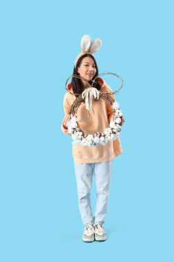 Mavi arka planda Paskalya çelengi olan tavşan kulaklı genç Asyalı kadın.