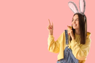 Tavşan kulaklı genç kadın pembe arka plandaki bir şeyi işaret ediyor. Paskalya kutlaması
