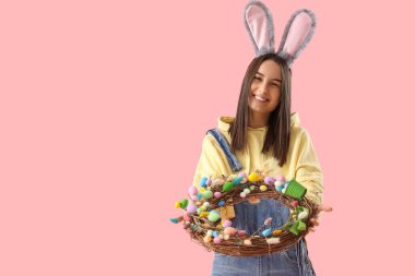 Pembe arka planda Paskalya çelengi olan tavşan kulaklı genç bir kadın.