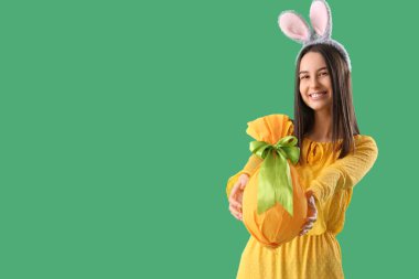 Yeşil arka planda Paskalya hediyesi yumurtası olan tavşan kulaklı genç bir kadın.