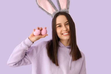 Leylak arka planında Paskalya yumurtaları olan tavşan kulaklı genç bir kadın.