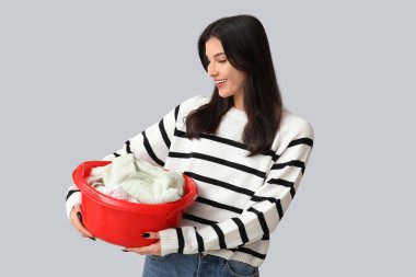 Gri arka planda temiz çamaşırları olan sepet tutan güzel bir genç kadın.