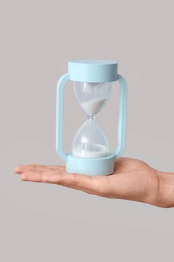 Gri arka planda kum saati tutan kadın.