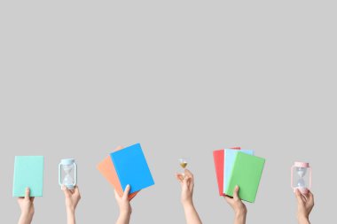 Kum saati tutan kadın eller ve gri arkaplan üzerine kitaplar