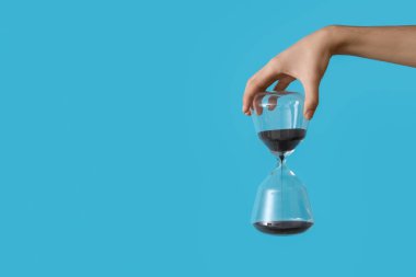 Mavi arka planda kum saati tutan kadın.