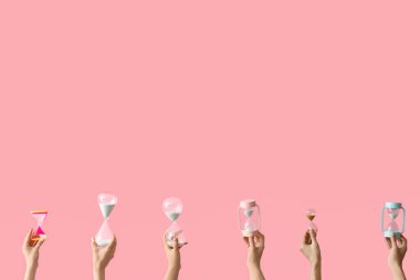 Pembe arka planda kum saati tutan kadın eller.