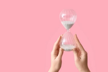 Female hands holding hourglass on pink background clipart