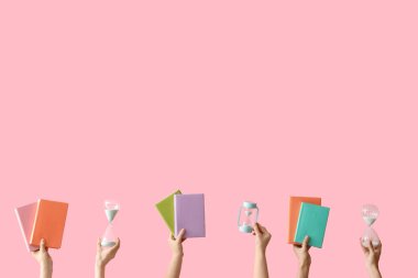 Kum saati tutan kadın eller ve pembe arka planda kitaplar.