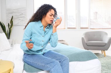 Yatak odasında astım spreyi kullanan Afro-Amerikalı genç bir kadın.