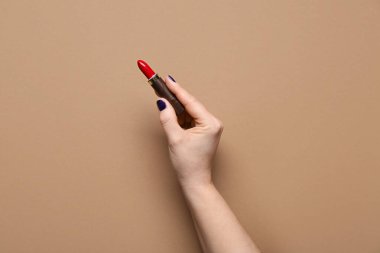 Kahverengi arka planda kırmızı ruj olan bir kadın eli.