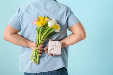 Hediye kutusu ve mavi arka planda bir buket güzel lalesi olan yakışıklı genç adam.