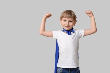 Gri arka planda süper kahraman gibi giyinmiş şirin küçük çocuk.