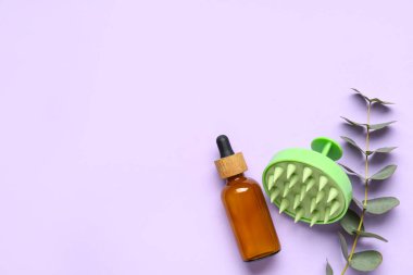 Saç derisi masaj aleti ve eflatun arka planında bir şişe kozmetik yağı ve okaliptüs.