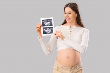 Işık arka planında sonogram görüntüsü olan güzel hamile kadın.