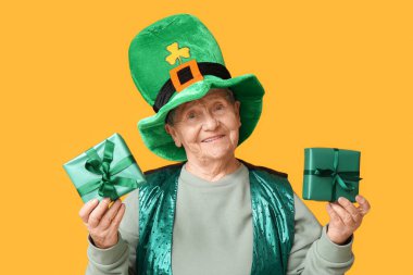 Sarı arka planda hediye kutuları olan cüce şapkalı yaşlı kadın. Aziz Patrick Günü kutlaması