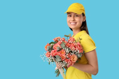 Mavi arka planda güzel çiçekleri olan genç teslimatçı kadın.