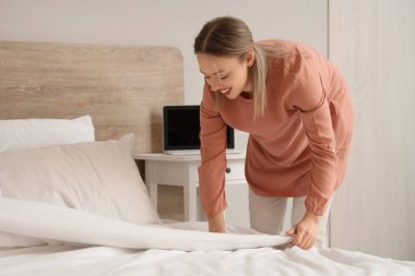 Güzel genç bir kadın hafif yatak odasında yatağını yapıyor.