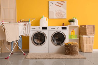 Çamaşır makinesi, kurutma makinesi ve temizlik malzemesi olan modern çamaşır odasının içi.