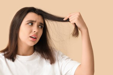 Kepek sorunu olan stresli genç bir kadın. Bej arka planda saçını inceliyor.