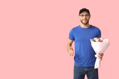 Bir buket güzel lalesi olan genç teslimatçı pembe arka planda baş parmak hareketi gösteriyor.