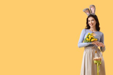 Sarı arka planda lale ve Paskalya yumurtaları olan tavşan kulaklı genç bir kadın.