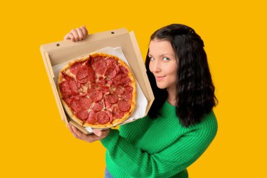 Sarı arka planda lezzetli pizzayla dolu karton bir kutu tutan güzel bir kadın.