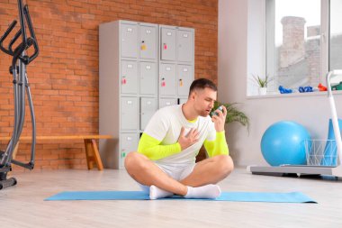 Sportif genç adam spor salonunda astım spreyi kullanıyor.