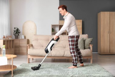 Genç adam oturma odasında halı temizliyor.