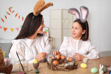 Küçük kız ve annesi tavşan kulaklı mutfakta Paskalya çelengi yapıyorlar.