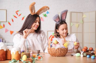 Küçük kız ve annesi tavşan kulaklı. Mutfakta paskalya yumurtası boyuyorlar.