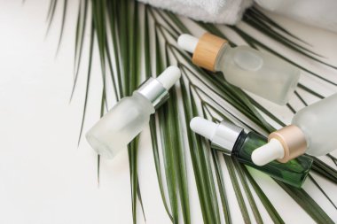 Beyaz masa üzerinde palmiye yaprağı olan kozmetik şişeleri, yakın plan.
