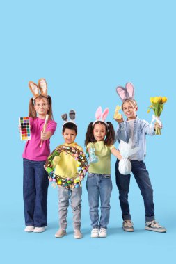 Paskalya desenli tavşan kulaklı küçük çocuklar ve mavi arka planda boyalar.