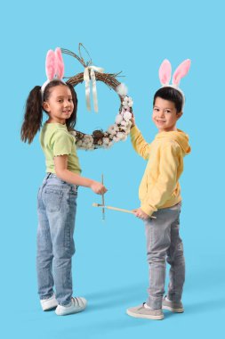 Paskalya çelengi takmış küçük Asyalı çocuklar ve mavi arka planda boya fırçaları.