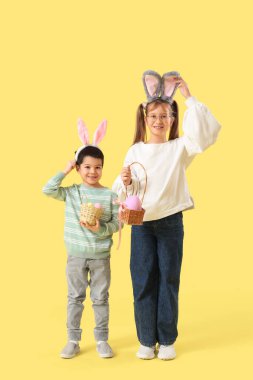 Sarı arka planda Paskalya yumurtaları olan tavşan kulaklı küçük çocuklar.