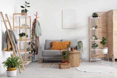 Raflarla, ev bitkileriyle, masa ve kanepelerle dolu rahat bir oturma odası.