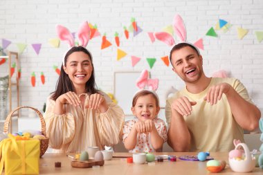 Tavşan kulaklı mutlu bir aile. Paskalya yumurtaları evde, masanın yanında oturuyor.