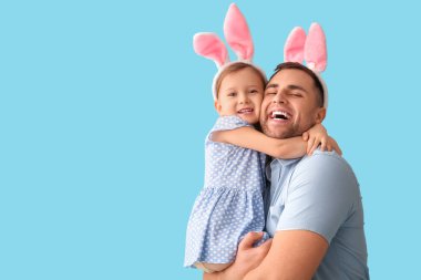 Küçük kızı olan mutlu genç bir adam. Mavi arka planda tavşan kulakları var.