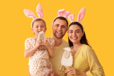 Paskalya tavşanı kulaklı mutlu bir aile. Sarı arka planda oyuncak koyunları var.