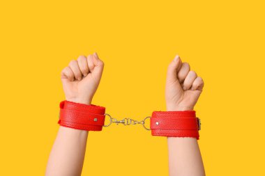 Sarı arka planda seks dükkanından kelepçelenmiş kadın elleri, yakın plan.