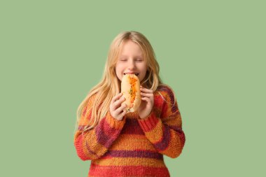 Tatlı küçük kız yeşil arka planda lezzetli sosisli yiyor.