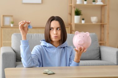 Evde anahtarı ve kumbarası olan hoşnutsuz genç bir kadın. İpotek kavramı