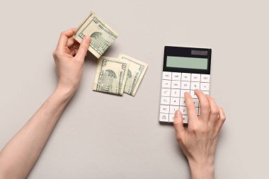 Gri arka planda hesaplamalar ve dolar banknotları yapan bir kadın. Borç kavramı
