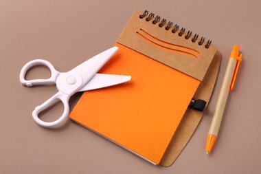 Kahverengi arkaplanda defter, kalem ve beyaz makas