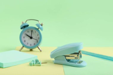 Çalar saat, zımba ve renk arkaplanındaki kırtasiye malzemeleri