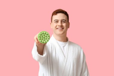 Pembe arka planda saç derisi masaj aleti olan genç bir adam.