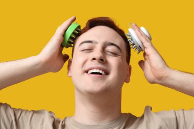 Sarı arka planda saç derisi masaj aleti kullanan genç bir adam.