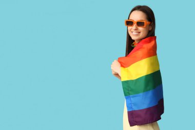 Mavi arka planda LGBT bayrağı olan güneş gözlüklü güzel bir kadın.