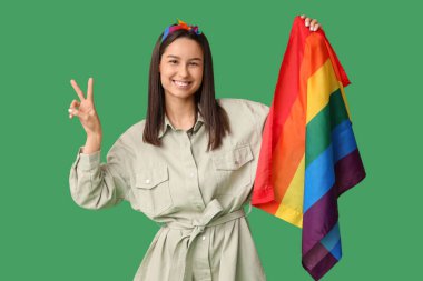 Yeşil arka planda zafer jesti gösteren LGBT bayrağıyla güzel genç bir kadın.