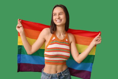 Beautiful young woman with LGBT flag on green background